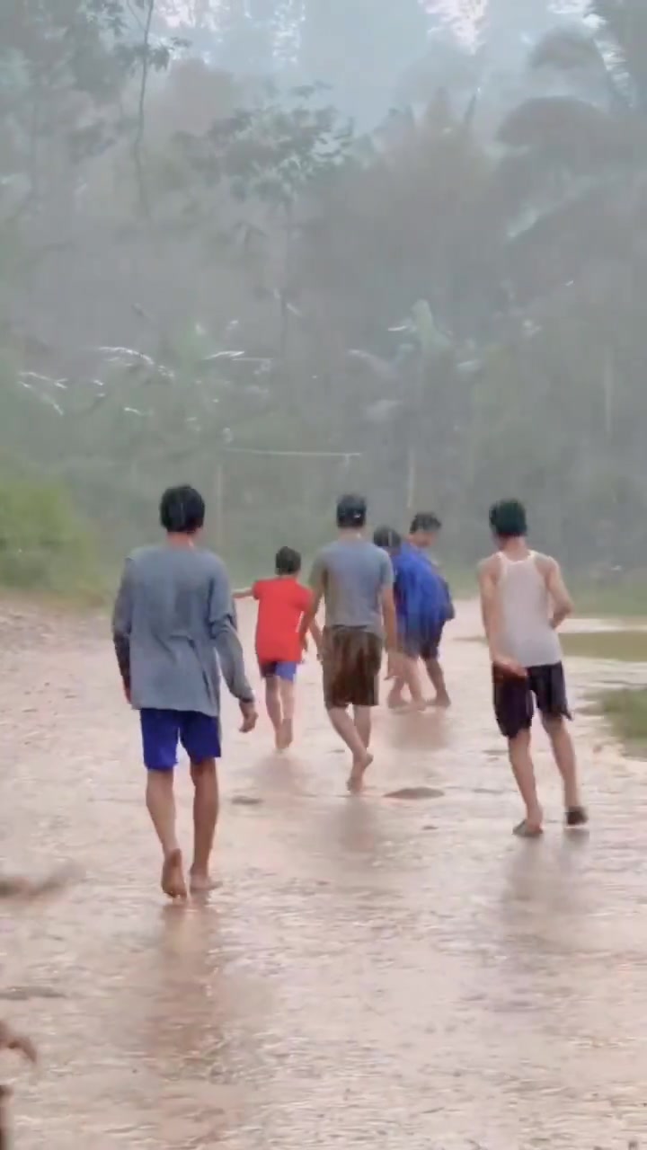 在磅礴大雨的泥地里踢球的小朋友们