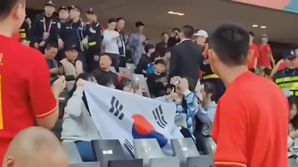 唉...国足球迷看台，几名女生举韩国国旗录像，一旁球迷神情无奈